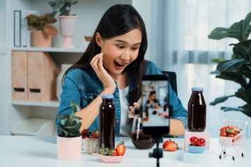 Smiling young beautiful Asian reviewing tasty mixed strawberry and cherry juice detox drinks,...