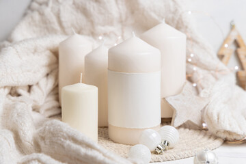 Pillar candle with label near white sweater and Christmas decor and baubles, mockup