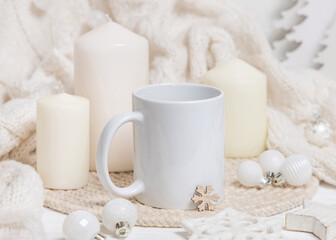 White blank coffee mug near candles, white sweater and Christmas decor, holiday mockup