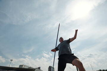 Athlete practicing pole vaulting on outdoor field with cityscape visible in background. Action...