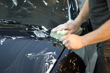 a hand with a washcloth and soap suds washes the hood of the car. Man washing car hood with...