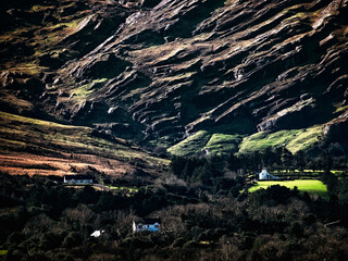 In a picturesque setting, small, white houses nestle among rolling green hills and rocky terrain...