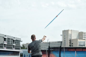 Person is participating in javelin throw event at sports stadium holding javelin in right hand with a stadium and buildings in background