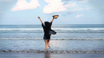 Joyful woman running on a beach while carrying a rattan hat
