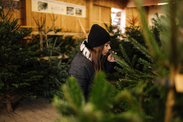 Elegant woman buys a Christmas tree. Woman in a black knited sweater. Beautiful lady choose fir tree