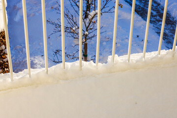 Snow-covered railing on villa balcony overlooking snowy tree in garden and pathway during bright winter day. Sweden.