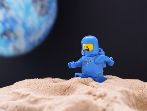 Tambov, Russian Federation - July 28, 2024 Lego astronaut minifigure walking on sand on a planet against a black space background with another blue planet in it