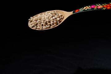 Pearl barley in a wooden spoon with an ornament on a dark background.