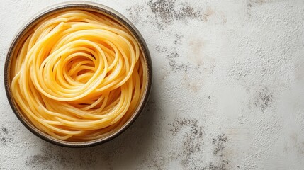 A bowl of cooked spaghetti arranged in a spiral on a textured surface.