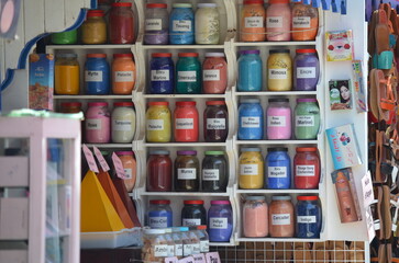 Display of vibrant pigments in glass jars at a shop in Essaouira, showcasing a wide range of traditional colors used in Moroccan art and crafts, adding a splash of color to the market scene

