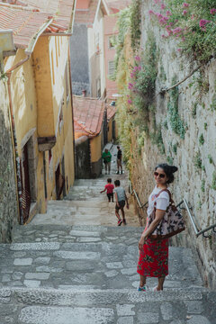 Fototapeta A beautiful female model with long black hair poses in the cobbled narrow stone streets of Porto with a trendy bag and in a vibrant outfit wearing sunglasses