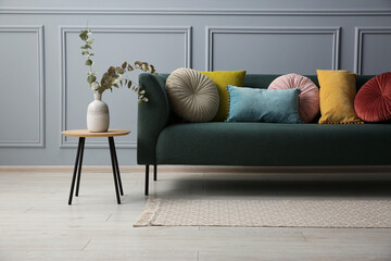 Stylish sofa with cushions and eucalyptus branches in vase on side table near grey wall