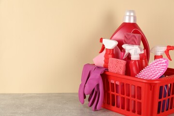 Different cleaning products and supplies in basket on grey table against beige background, space for text