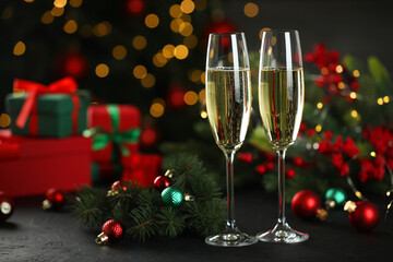 Champagne in glasses and decor on black table against blurred Christmas lights, space for text