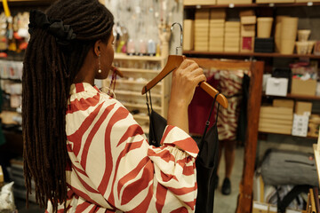 Individual browsing and examining clothes in busy retail shop with various items in background....