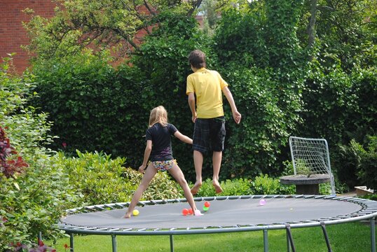 View behind a boy and a girl jumping on a trampoline in Randers, Denmark in summertime.