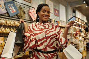 Woman wearing zebra-print dress standing in store while holding shopping bags and credit card,...