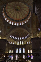 Obraz premium The interior dome of a mosque in Istanbul, adorned with intricate Islamic calligraphy and colorful stained glass windows. The soft lighting enhances the rich patterns and architectural grandeur 