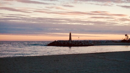 Fototapeta premium Coastal Sunset with Breakwater Lighthouse and Calm Ocean