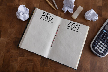 Pro and contra concept. Laptop, magnifying glass, pen, spectacle and a note book written with text Pros and Cons on white office desk table.Top view shot of creative lay out with copy space.