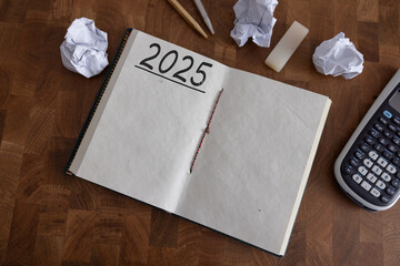 New year resolutions 2025 on desk. 2025 goals list with notebook, tea cup, pen, plant on wooden...