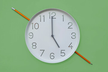 Clock and pencil. Round white wall clock shows 5 o'clock on plain green background copy space....