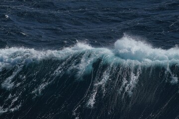 Powerful ocean wave crashing with white foam against dark blue water, showcasing beauty and force of nature