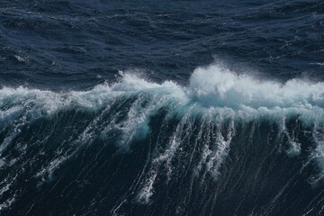 Ocean wave crashing with frothy white foam against deep blue water, showcasing power and beauty of nature