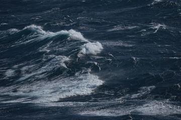 Dynamic ocean waves crashing against each other, creating dramatic seascape. deep blue water contrasts with white foam, evoking sense of power and movement