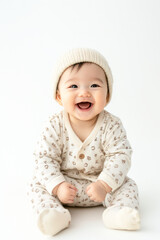 Asian baby in pajamas and cap sitting and smiling. Isolated on white background.