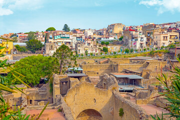The photo shows a view of Herculaneum, capturing the ancient Roman ruins with well-preserved buildings, stone streets, and remnants of daily life, set against a backdrop of lush greenery.