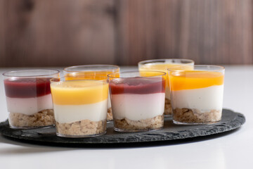 Dessert Shots, Cheesecake in glasses with raspberry and mango topping, desserts on a black stand and white background, in various pannacotta