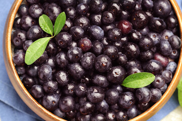 Ripe acai berries and leaves in bowl on table, top view