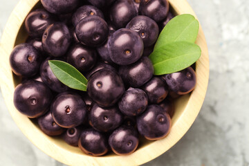 Ripe acai berries and leaves in bowl on grey table, top view