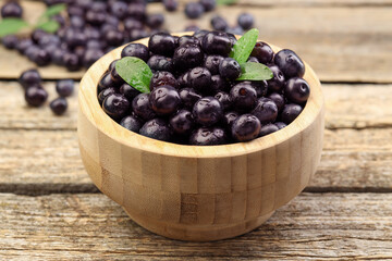 Ripe acai berries and leaves in bowl on wooden table, closeup