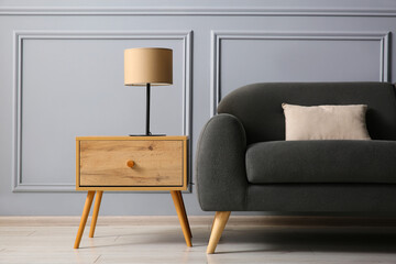 Stylish sofa with cushion and lamp on side table near grey wall
