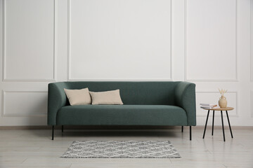 Stylish sofa, pillows and side table with decor near white wall indoors