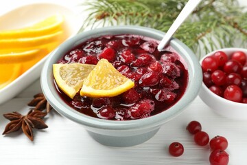 Tasty cranberry sauce in bowl, berries, orange, anise and fir tree branches on white wooden table, closeup