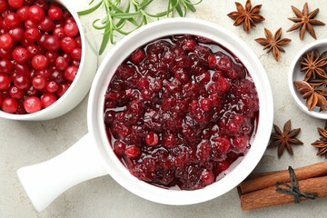 Tasty cranberry sauce in gravy boat, honey, spices and berries on light table, top view