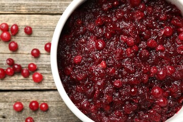 Tasty cranberry sauce in saucepan and berries on wooden table, top view