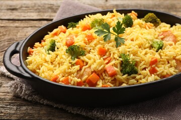 Tasty rice with vegetables in baking dish on wooden table, closeup