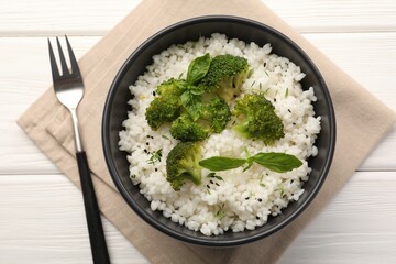 Tasty rice with broccoli and basil in bowl on white wooden table, top view