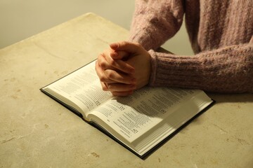 Naklejka premium Woman with open Holy Bible in English language praying at beige table, closeup