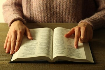 Naklejka premium Woman reading Holy Bible in English language at wooden table, closeup