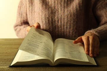 Fototapeta premium Woman reading Holy Bible in English language at wooden table, closeup