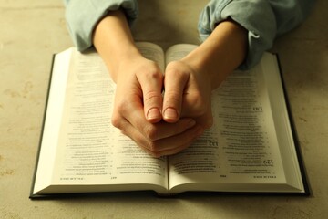 Woman with open Holy Bible in English language praying at beige table, closeup