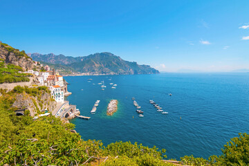 The photo captures a sunny view of Amalfi, showcasing the town's colorful buildings, steep cliffs,...