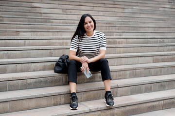 Happy and cheerful woman sitting on concrete stairs outdoors