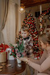 Cute kid decorates Christmas tree with toys with his mother