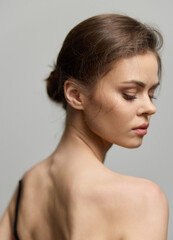 Obraz premium Elegant young woman with natural beauty posing gracefully against a soft neutral background. Hair styled in a bun, showcasing a serene and contemplative expression.